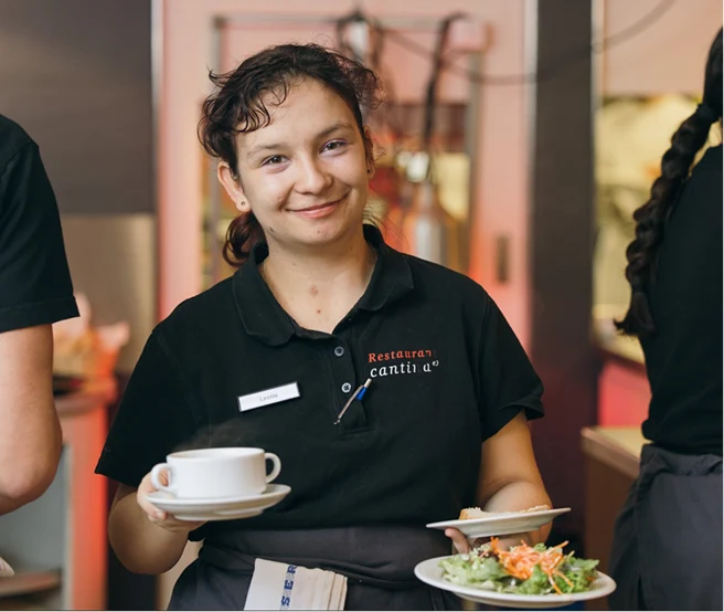 Lächelnde Servicemitarbeiterin hält eine Tasse und einen Teller mit Salat im Restaurant