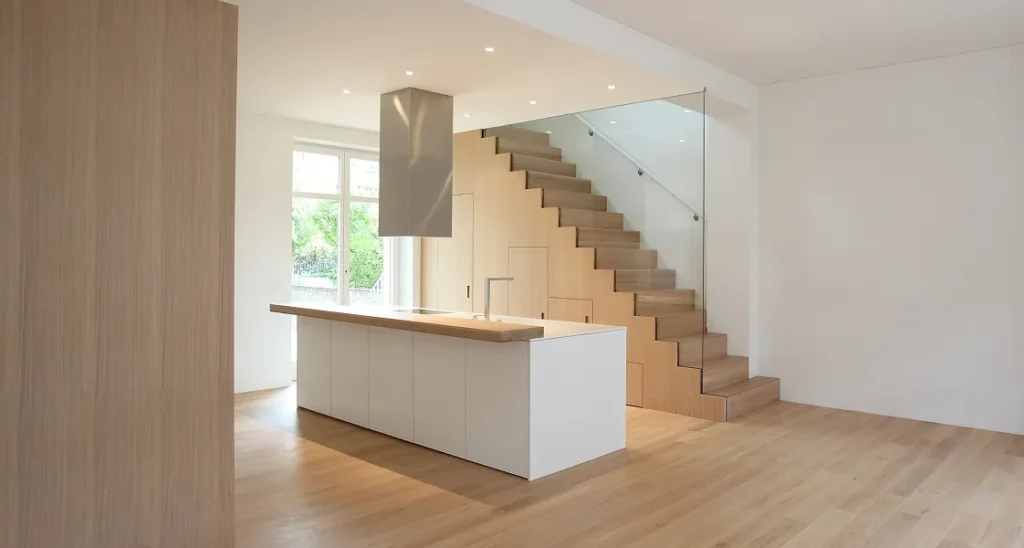 Moderne Küche mit weisser Kücheninsel und Holztreppe mit Glasgeländer
