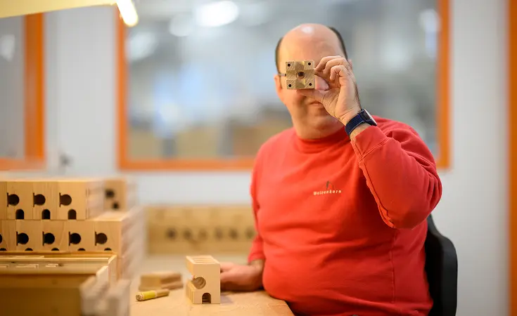 Mann sitzt an einem Werktisch mit kleinen Holzstücken in der Werkstatt