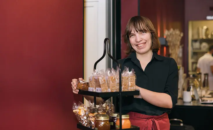Lächelnde Mitarbeiterin hält ein Tablett mit Süssgebäck im Restaurant