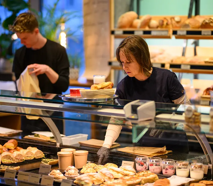 Zwei Mitarbeitende an der Theke einer Bäckerei mit Brot und Gebäck